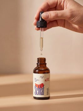 Verpackungsdesign für die Selfcare-Marke Grinsekatzen – Hand mit Pipette über einer CBD-Tropfflasche Schlaf mit individueller Illustration und markanter Typografie.