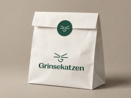 Branding für die Selfcare-Marke Grinsekatzen – weiße Papiertüte mit grünem Logo und rundem Verschlusssticker mit Bildmarke
